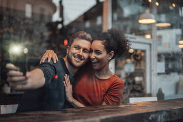 Cheerful couple taking selfie through mobile phone while sitting at cafe - JOSEF03573