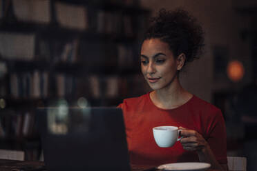 Junge Frau trinkt Kaffee und arbeitet am Laptop im Café - JOSEF03584