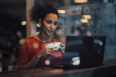 Junge Frau mit Kaffeetasse, die im Café sitzend am Laptop arbeitet - JOSEF03589