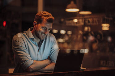 Lächelnder Geschäftsmann, der einen Laptop benutzt, während er in einem Café sitzt - JOSEF03597