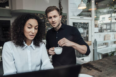 Geschäftsmann kocht Kaffee, während er mit einem Kollegen am Laptop in einem Café arbeitet - JOSEF03603