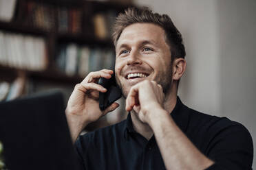 Mid adult businessman smiling while talking on mobile phone siting at cafe - JOSEF03608