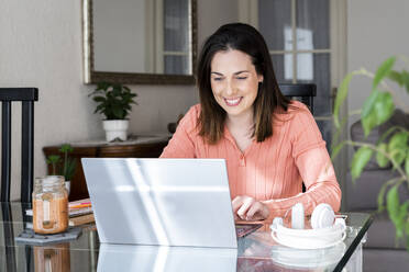 Smiling businesswoman working on laptop at home office - AFVF08168