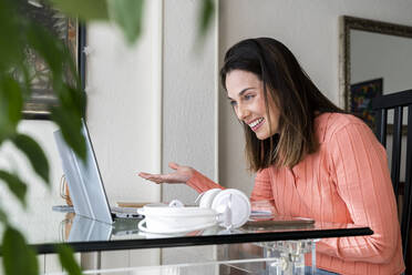 Happy businesswoman gesturing during video call while sitting at table in home office - AFVF08176