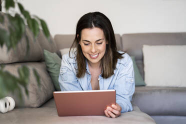 Smiling woman using tablet while relaxing on sofa at home - AFVF08182