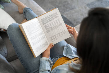 Woman reading book while relaxing on sofa at home - AFVF08193