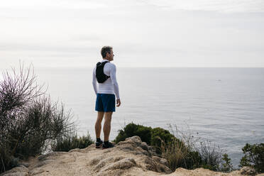 Mature man standing at mountain cliff near sea against clear sky - JRFF05066