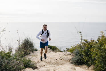 Man running on mountain near sea against cloudy sky - JRFF05070