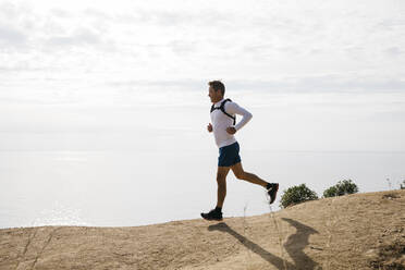 Man running on dirt road against cloudy sky during sunny day - JRFF05084