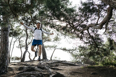 Männlicher Läufer, der beim Laufen im Wald über Wurzeln springt - JRFF05093