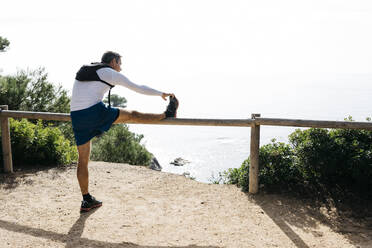 Man stretching on wooden railing during sunny day - JRFF05094