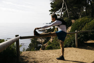 Mature man stretching near wooden railing near forest - JRFF05095