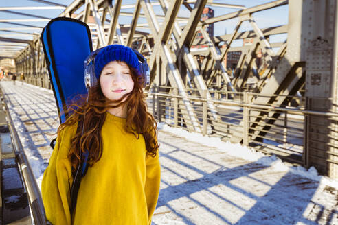Mädchen mit geschlossenen Augen hört Musik über Kopfhörer, während sie auf einer Brücke steht - IHF00416