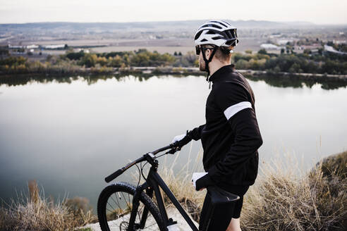 Sportsman with bicycle standing at river - EBBF02510