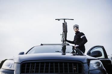 Sportler, der sein Fahrrad auf dem Autodach hält und in den Himmel schaut - EBBF02514