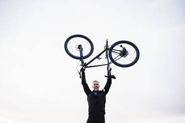 Fröhlicher Sportler hebt Fahrrad gegen den Himmel - EBBF02517