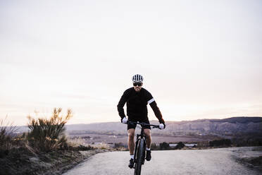 Männlicher Radfahrer fährt Fahrrad gegen den Himmel bei Sonnenuntergang - EBBF02519