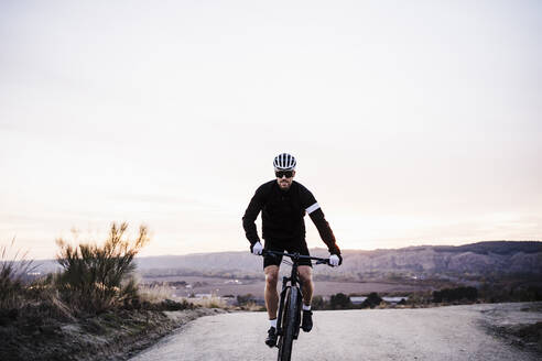 Male biker riding bicycle against sky during sunset - EBBF02519