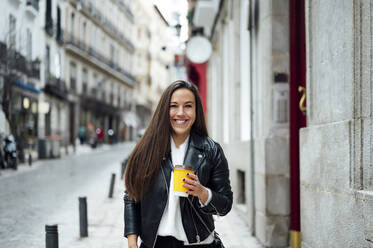 Mid adult woman holding reusable cup while standing at street in city - PGF00462