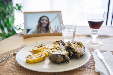 Mittagessen am Tisch, während Frau auf dem Bildschirm eines digitalen Tablets zu sehen ist, lizenzfreies Stockfoto