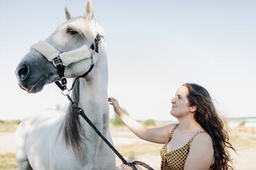 Smiling young woman with horse at equestrian center against clear sky - MRRF00892