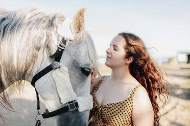 Junge Frau streichelt Pferd im Reitsportzentrum gegen den klaren Himmel - MRRF00893