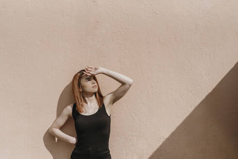 Beautiful redhead woman standing against wall while looking away - DSIF00343