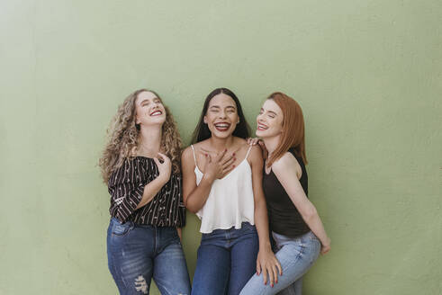 Unbeschwerte junge Frauen, die lachend an einer grünen Wand stehen - DSIF00355