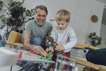 Vater spielt mit seinem Sohn, während er auf dem Sofa im Wohnzimmer sitzt - MFF07150