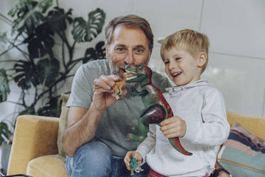 Smiling father and son playing with dinosaur toys - MFF07152