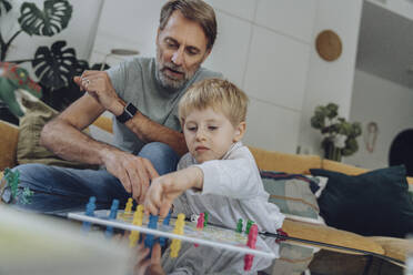 Älterer Mann spielt mit seinem Sohn ein Brettspiel, während er im Wohnzimmer sitzt - MFF07153