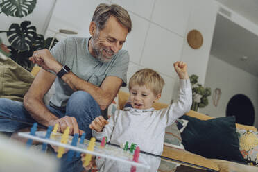 Happy boy playing board game with father in living room - MFF07154