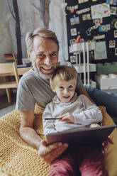 Lächelnder Vater und Sohn mit digitalem Tablet im Schlafzimmer - MFF07169