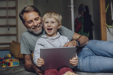 Lächelnder Vater und Sohn verwenden Tablet im Schlafzimmer - MFF07182
