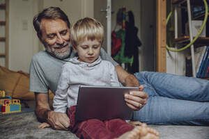 Lächelnder Vater mit Sohn, der im Schlafzimmer ein Tablet benutzt - MFF07184