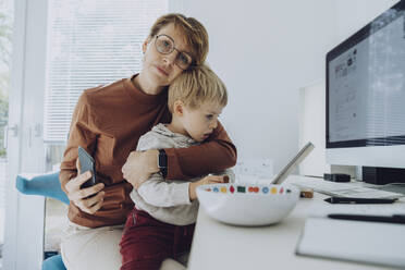Affectionate mother embracing son watching digital tablet at home office - MFF07188