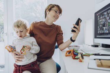 Mutter benutzt ihr Smartphone, während ihr Sohn auf dem Schoß sitzt und mit Spielzeug spielt - MFF07194