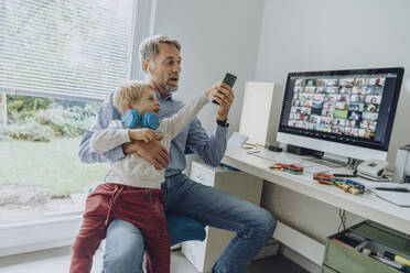 Sohn lenkt Vater bei Videokonferenz im Home Office mit Smartphone ab - MFF07200