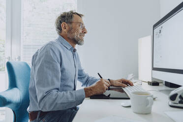 Geschäftsmann beim Schreiben auf einem digitalen Tablet während der Arbeit im Büro zu Hause - MFF07209