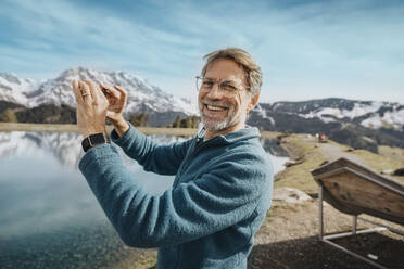 Lächelnder reifer Mann beim Fotografieren der Aussicht am Hochkonig, Salzburger Land, Österreich - MFF07217