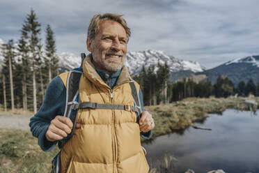 Smiling mature man with backpack standing against sky at Salzburger Land, Austria - MFF07230