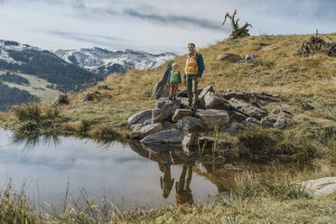 Älterer Mann mit Sohn auf einem Felsen an einem Teich vor dem Himmel im Salzburger Land, Leoganger Berge, Österreich - MFF07233