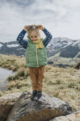Boy holding sunglasses while standing on rock against sky at Salzburger Land, Leogang Mountains, Austria - MFF07235