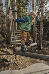 Boy holding rope while walking on wood in forest at Salzburger Land, Austria - MFF07242