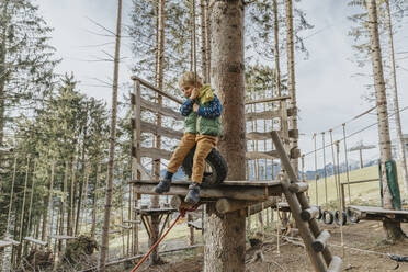 Verspielter Junge, der sich im Wald im Salzburger Land an ein Seil hängt, Österreich - MFF07245
