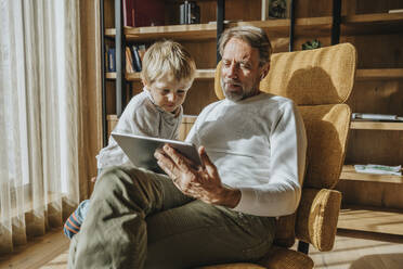Curious boy looking while father using digital tablet at home - MFF07278