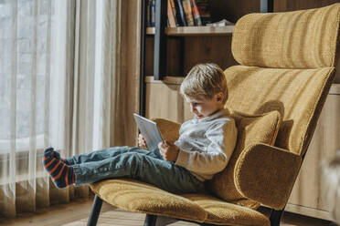 Boy e-learning while sitting on chair in living room - MFF07281