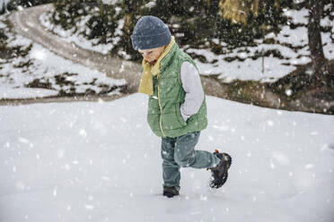 Junge in warmer Kleidung spielt im Schnee, während es im Winter schneit - MFF07296
