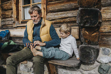 Vater hilft seinem Sohn beim Anziehen der Socken, während er an der Hütte sitzt - MFF07303
