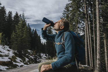 Männlicher Tourist trinkt Wasser, während er an einem Baum im Salzburger Land, Österreich, sitzt - MFF07312